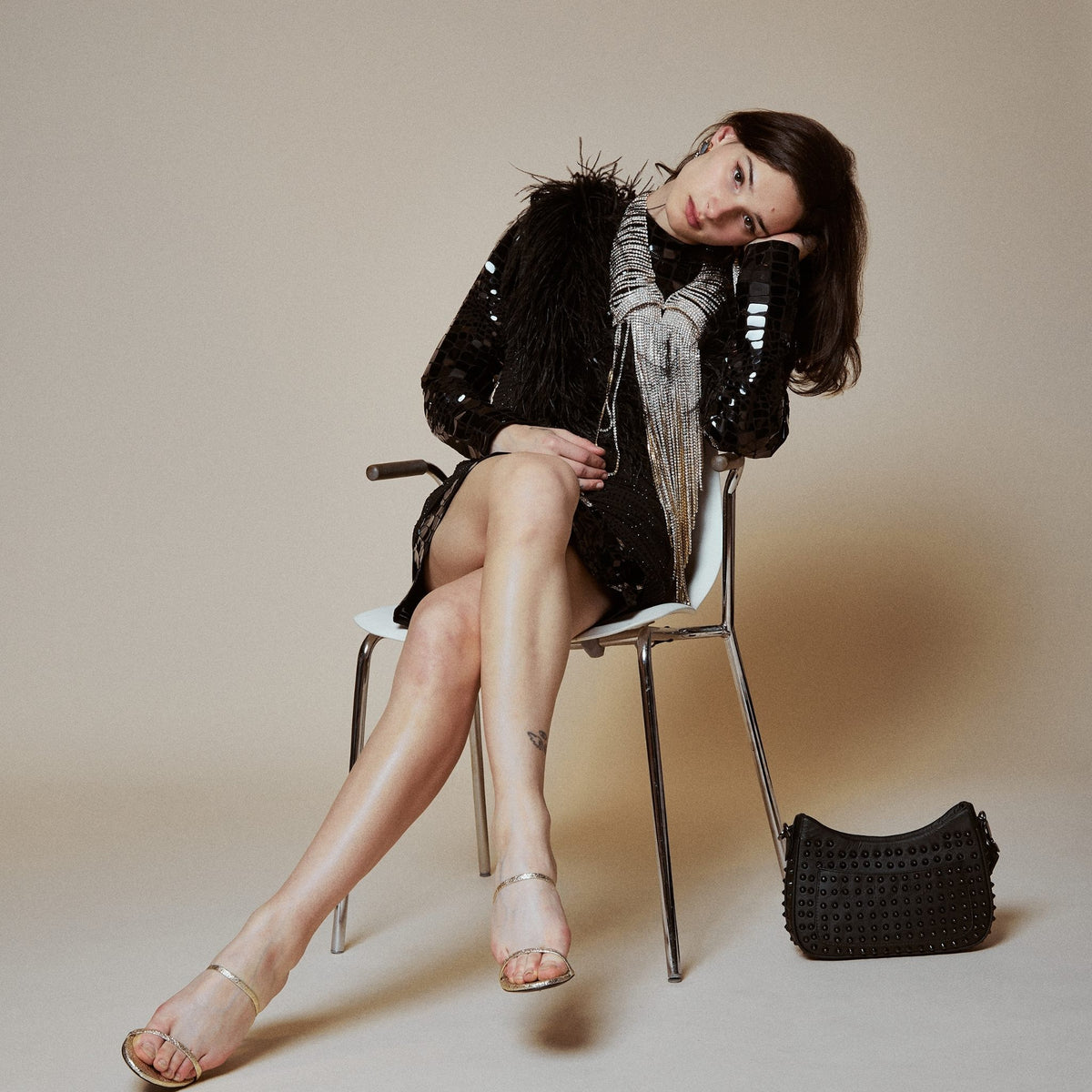 Woman sitting on a chair with a black handbag beside her against a beige background