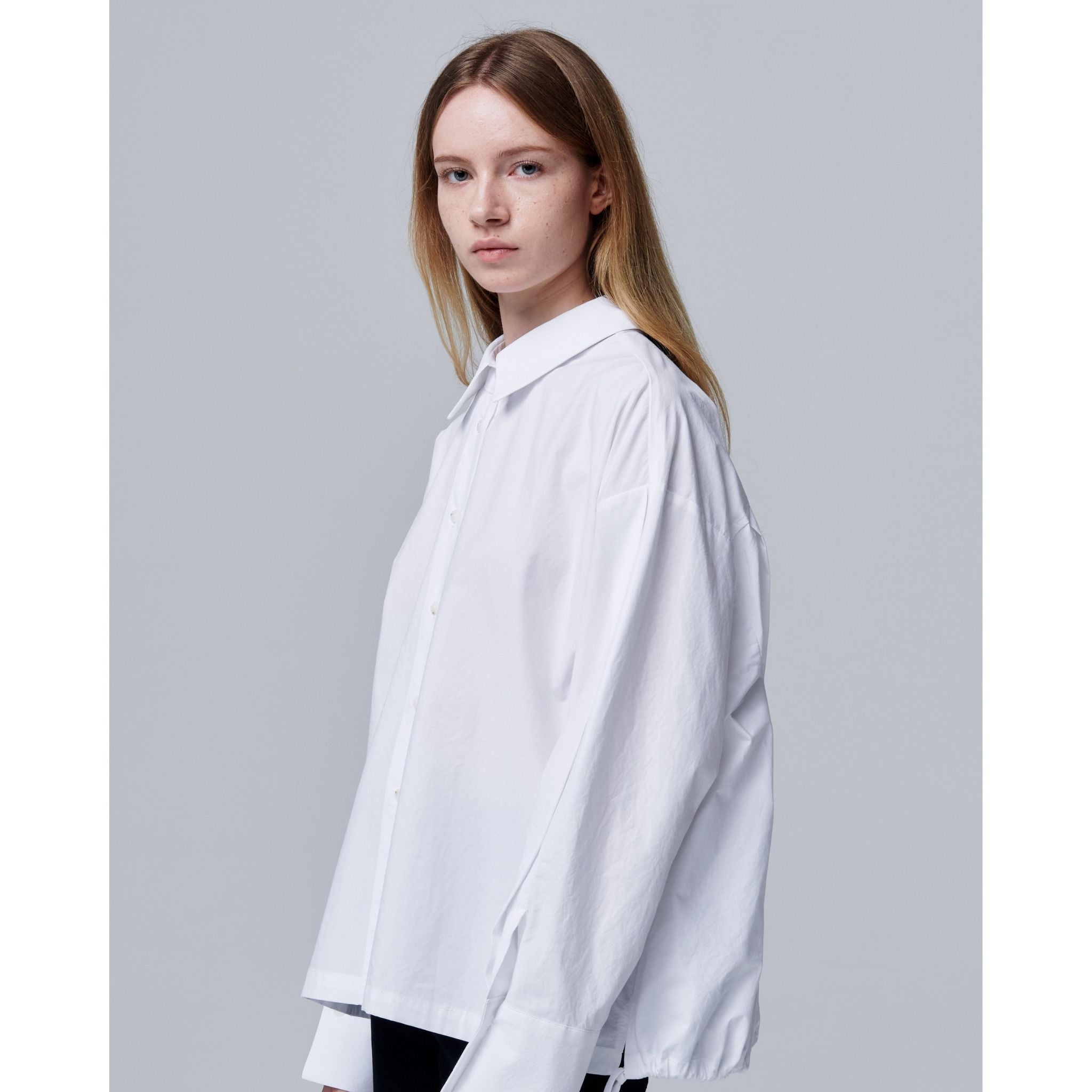 Woman wearing a white oversized shirt against a plain background