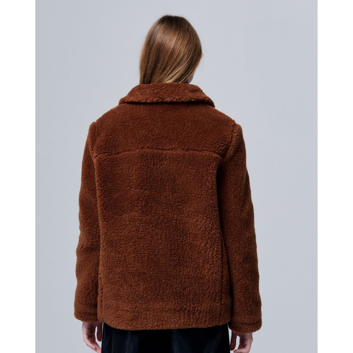 A person with long, light brown hair faces away from the camera, wearing the Ethereal Fur Jacket with Soft Fleece Fabric and dark pants against a plain light gray background.