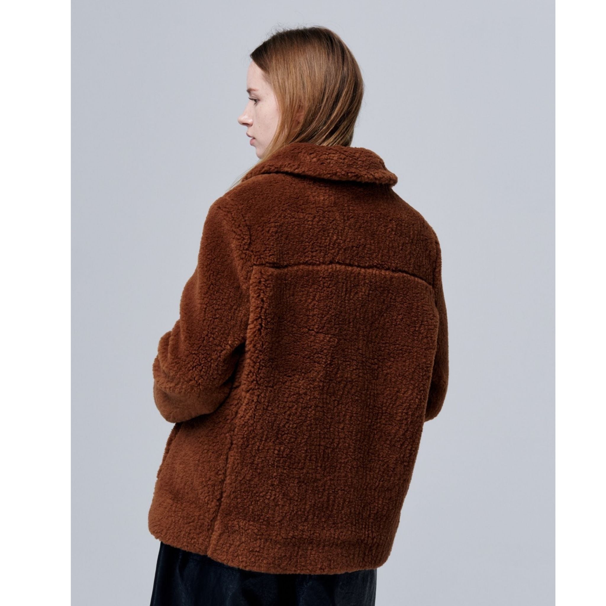 A person with long brown hair, viewed from the side and back, wears the Ethereal Fur Jacket with Soft Fleece Fabric—an ideal winter layering piece—set against a plain light gray background.