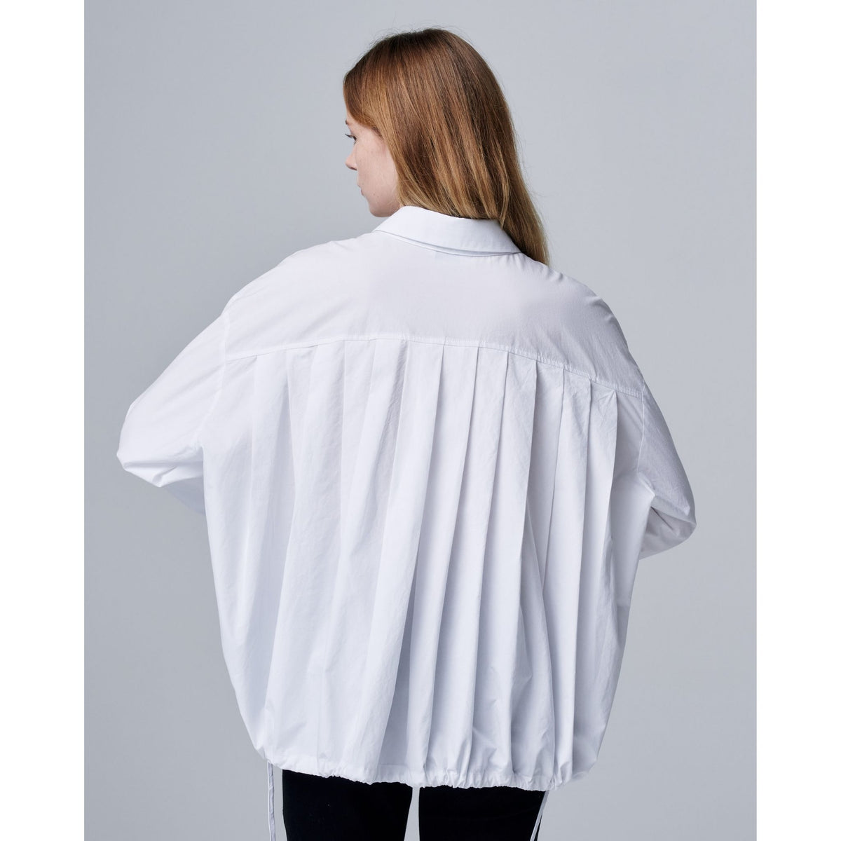 Person wearing a white oversized shirt against a plain background
