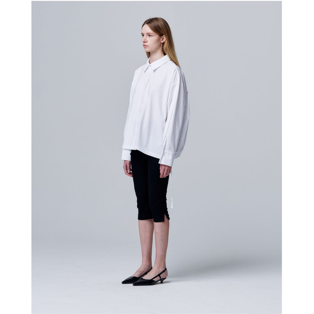 Person wearing a white oversized shirt and black pants on a light gray background