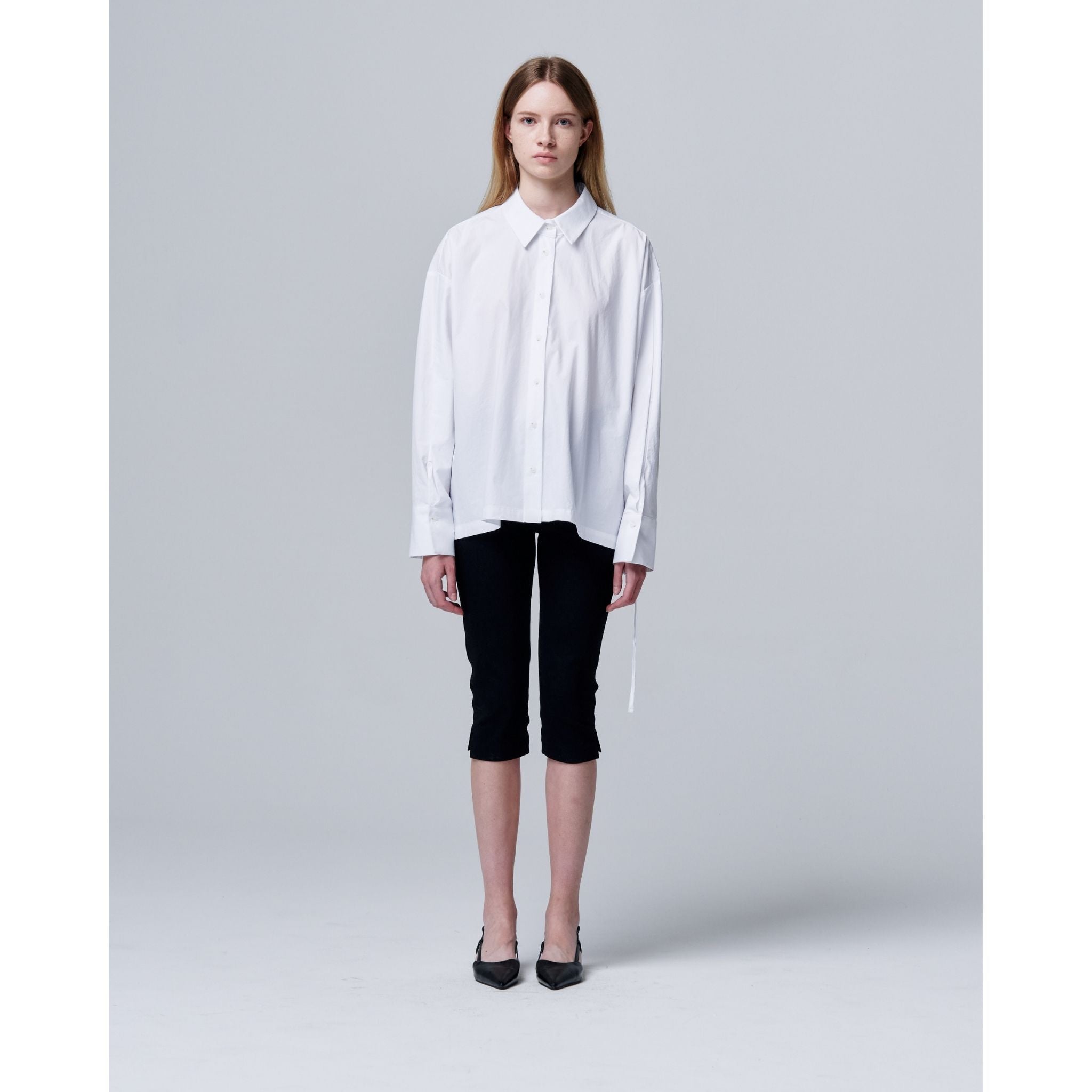 Woman wearing a white shirt and black pants on a gray background