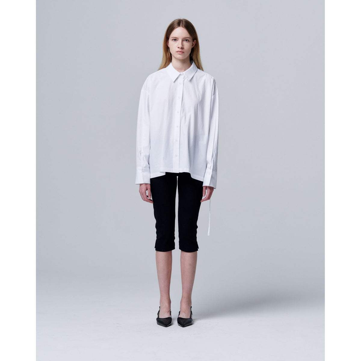 Woman wearing a white shirt and black pants on a gray background