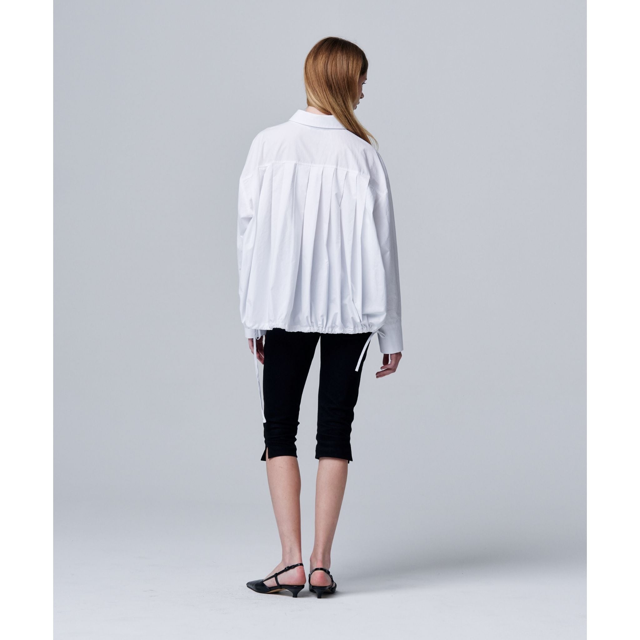 Person wearing a white shirt and black pants on a plain background