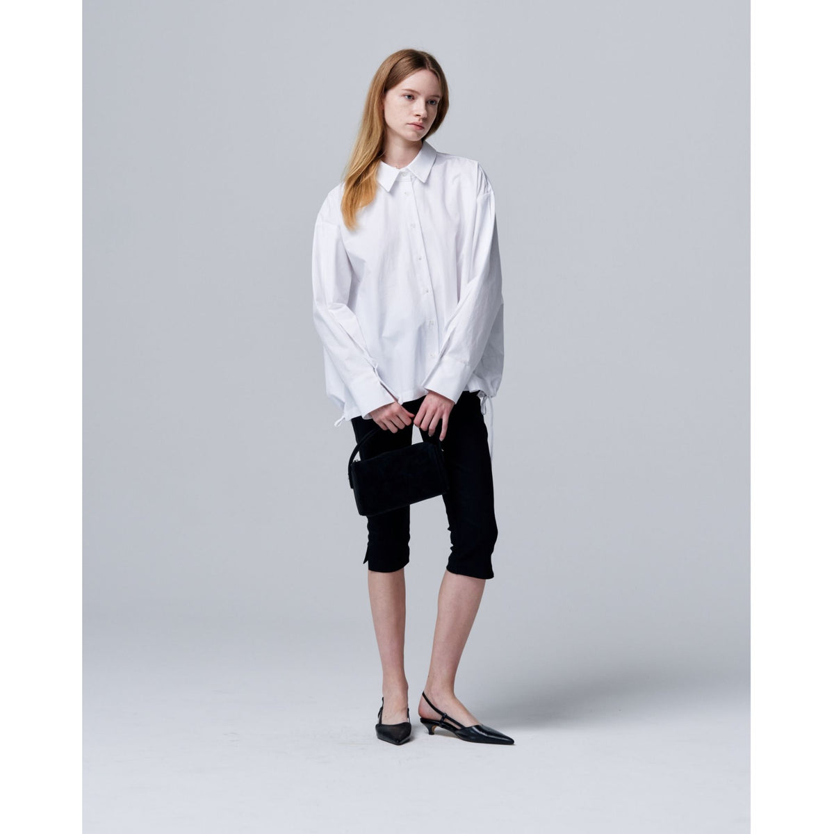 Woman wearing a white blouse and black pants on a plain background