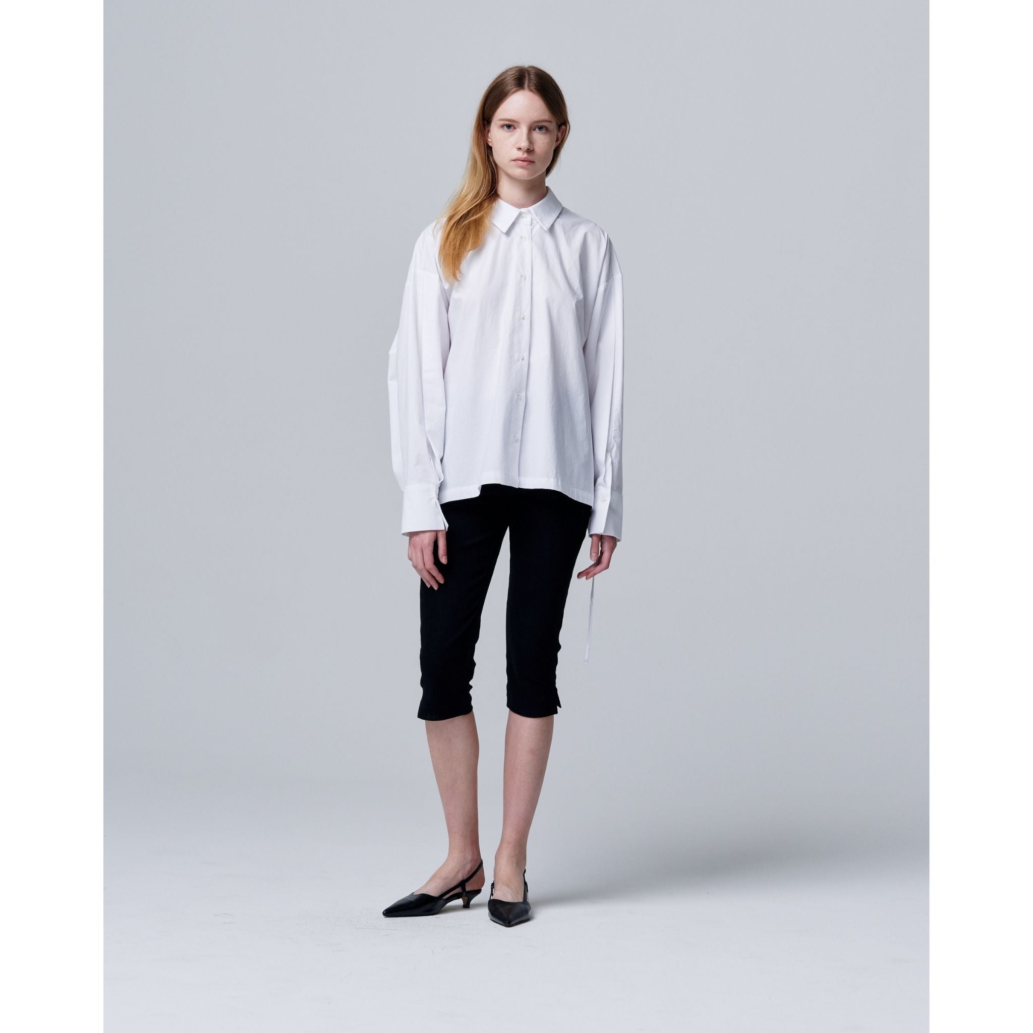 Woman wearing a white shirt and black pants on a gray background