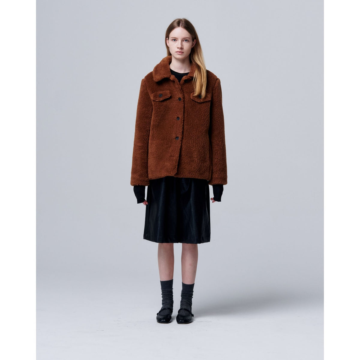 Person wearing a brown coat and black skirt on a plain background