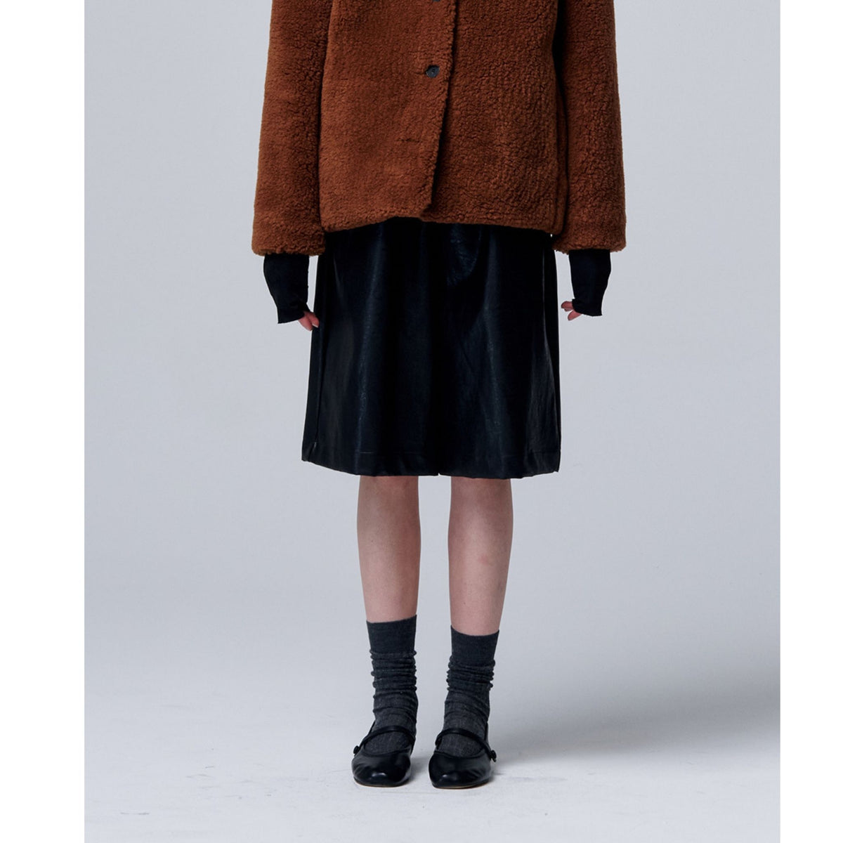 Person wearing a brown coat, black skirt, and black shoes on a white background