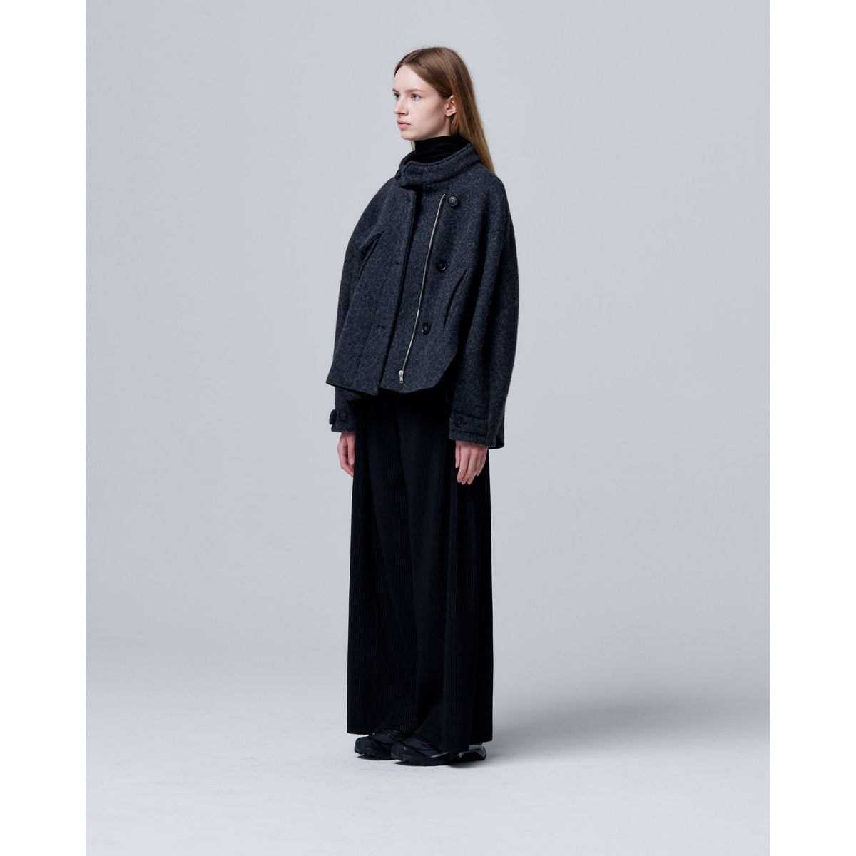 Woman wearing a dark gray jacket and black pants on a light gray background