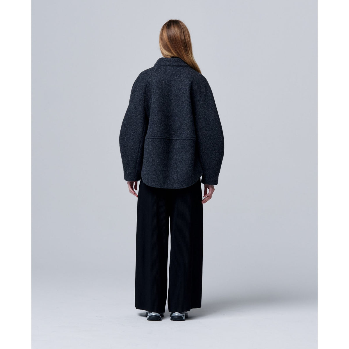 Person wearing a dark gray coat and black pants on a light gray background