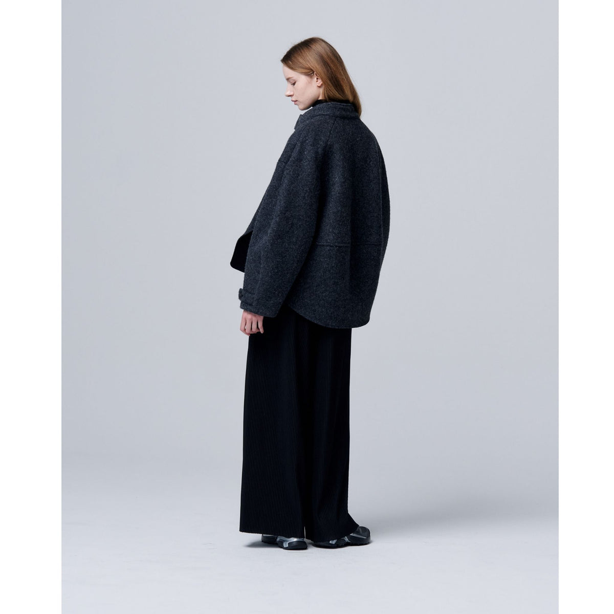 Person wearing a dark gray coat and black pants on a light gray background