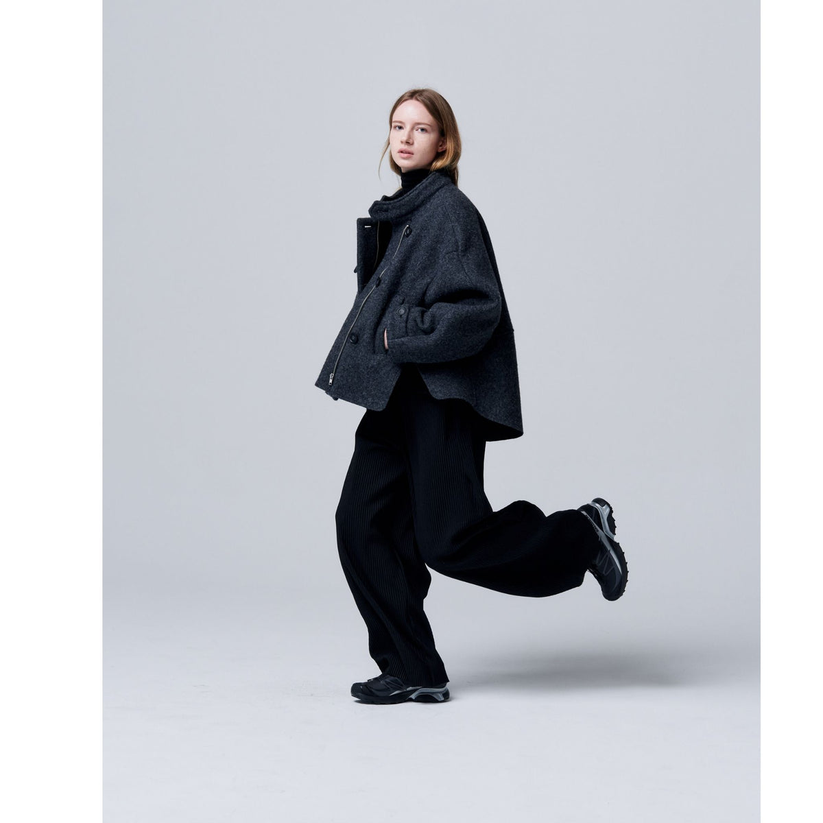 Person wearing a dark coat and pants on a light gray background