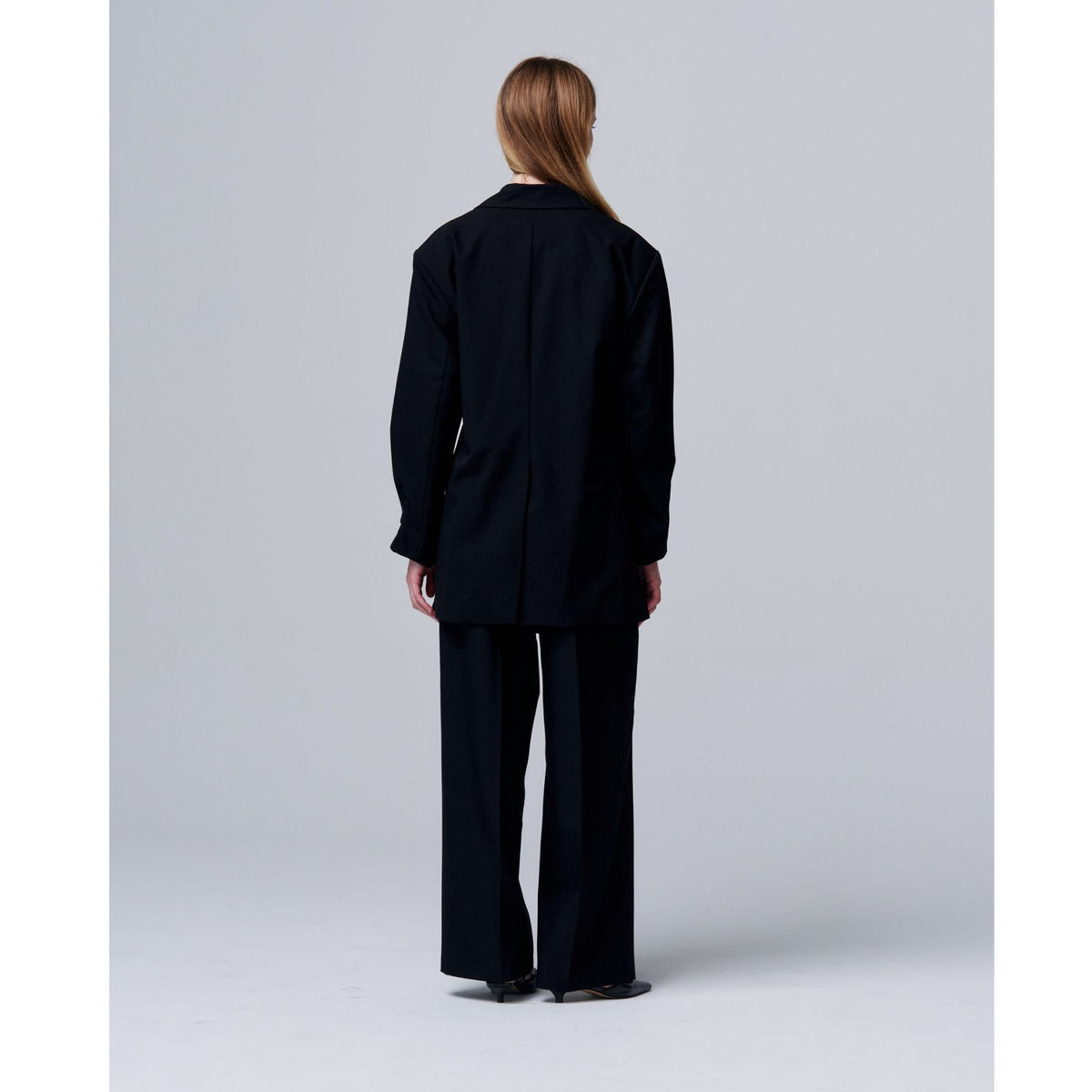 Person wearing a black suit standing against a plain background