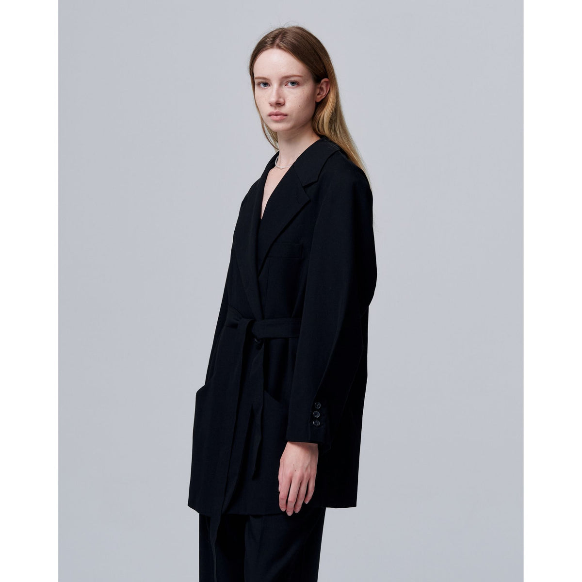 Person wearing a black suit against a plain background