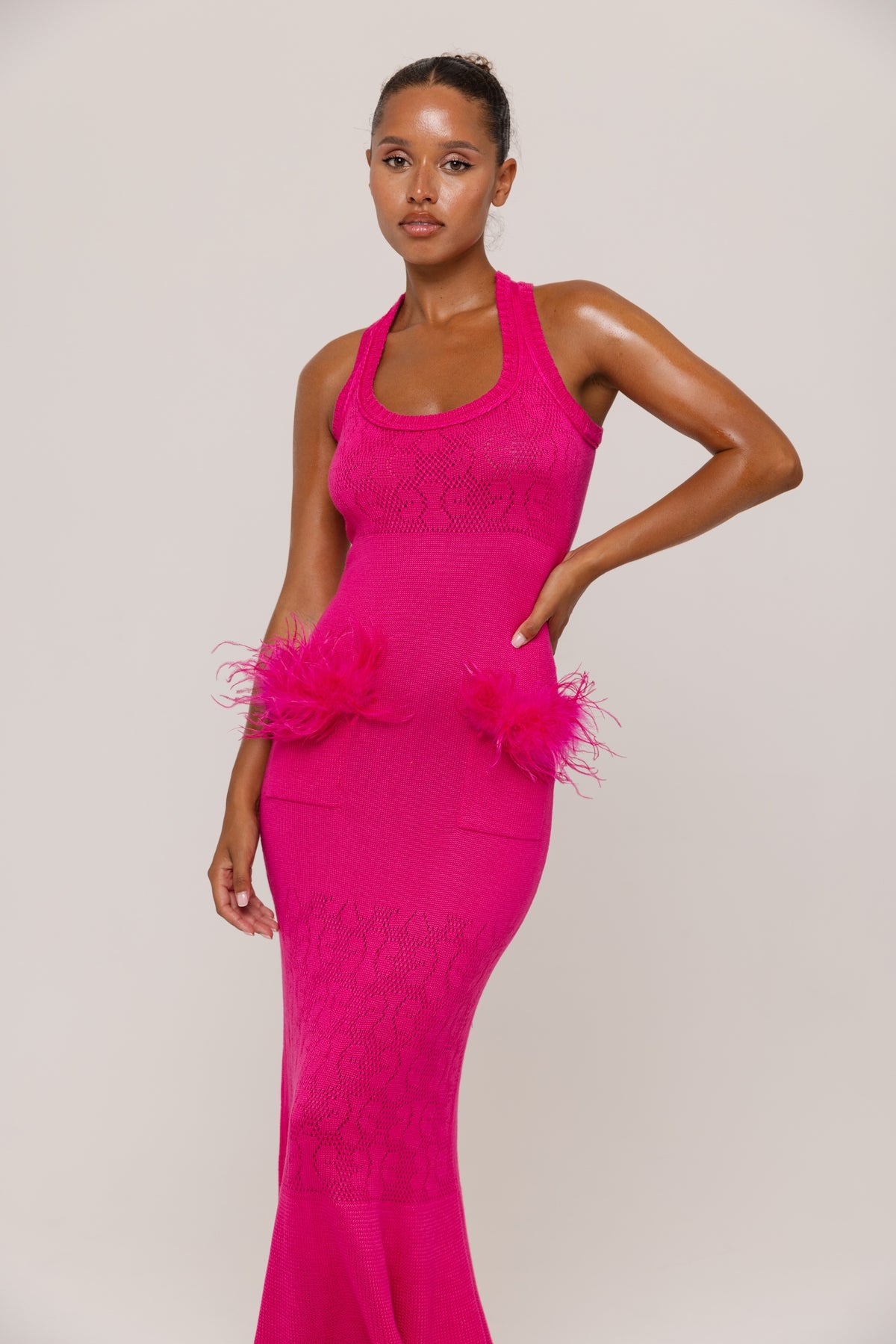 Woman wearing a fuchsia  dress with feather details on a plain background
