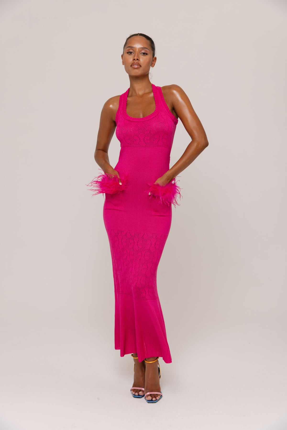 Woman wearing a fuchsia dress with feathered details on a plain background