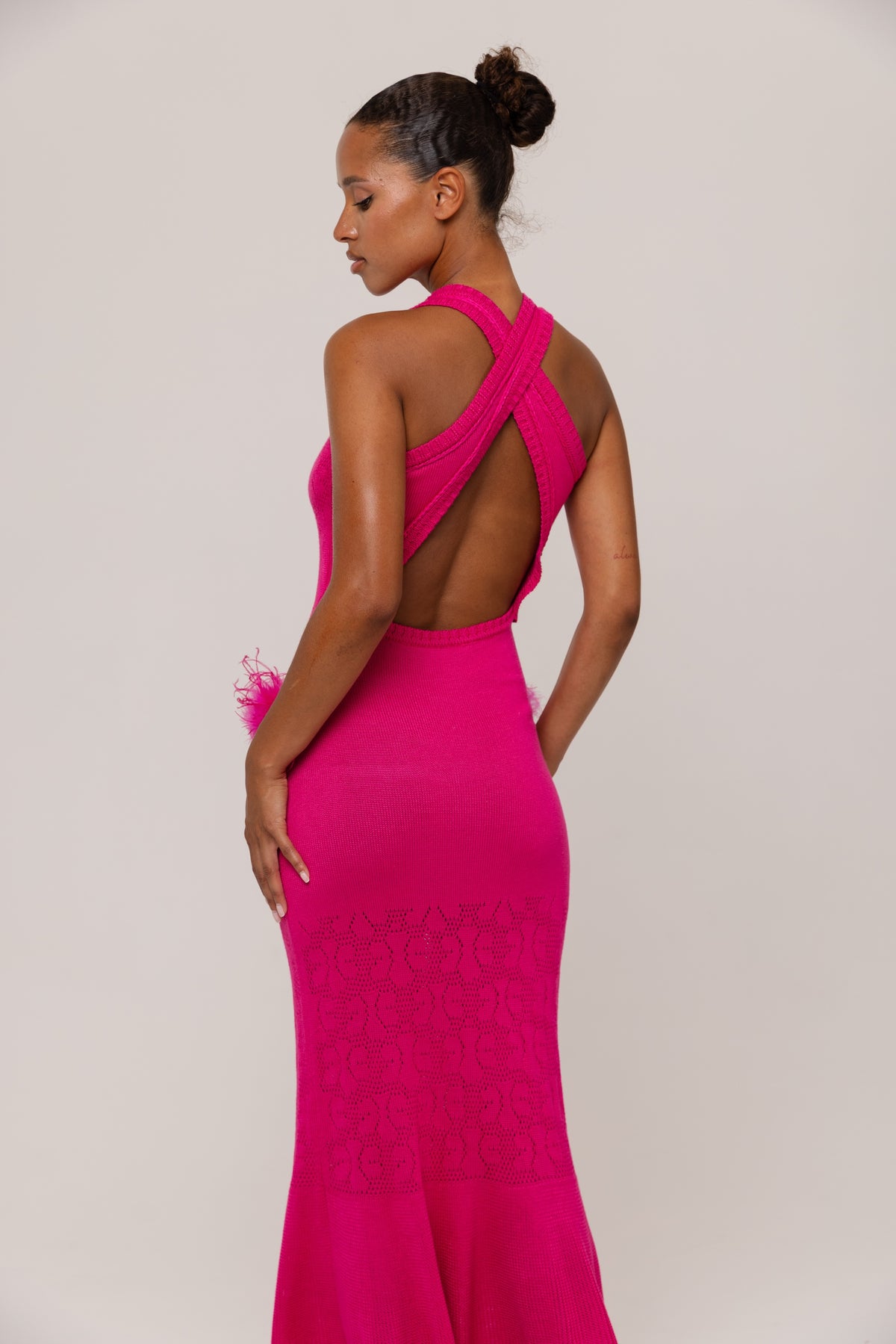 Woman wearing a fuchsia evening gown with a open back on a plain background
