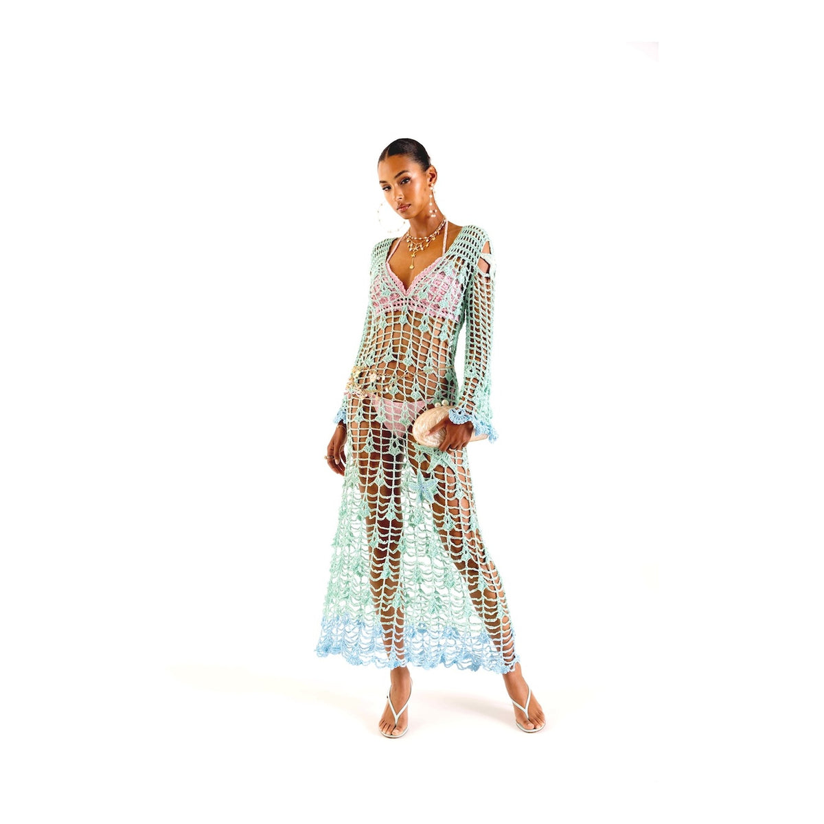 A woman wears the Aqua Marine Handmade Maxi Cover-Up Dress by ANDREEVA over a bikini, paired with sandals and a seashell clutch, against a plain white background.