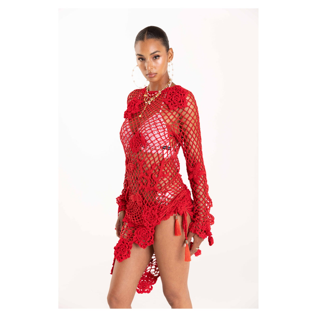 A woman models the ANDREEVA Cherry Handmade Crochet Top—a red, long-sleeve cotton piece with floral details—styled with large hoops and a gold chain, ideal as a cover-up or beach layer, against a plain white background.