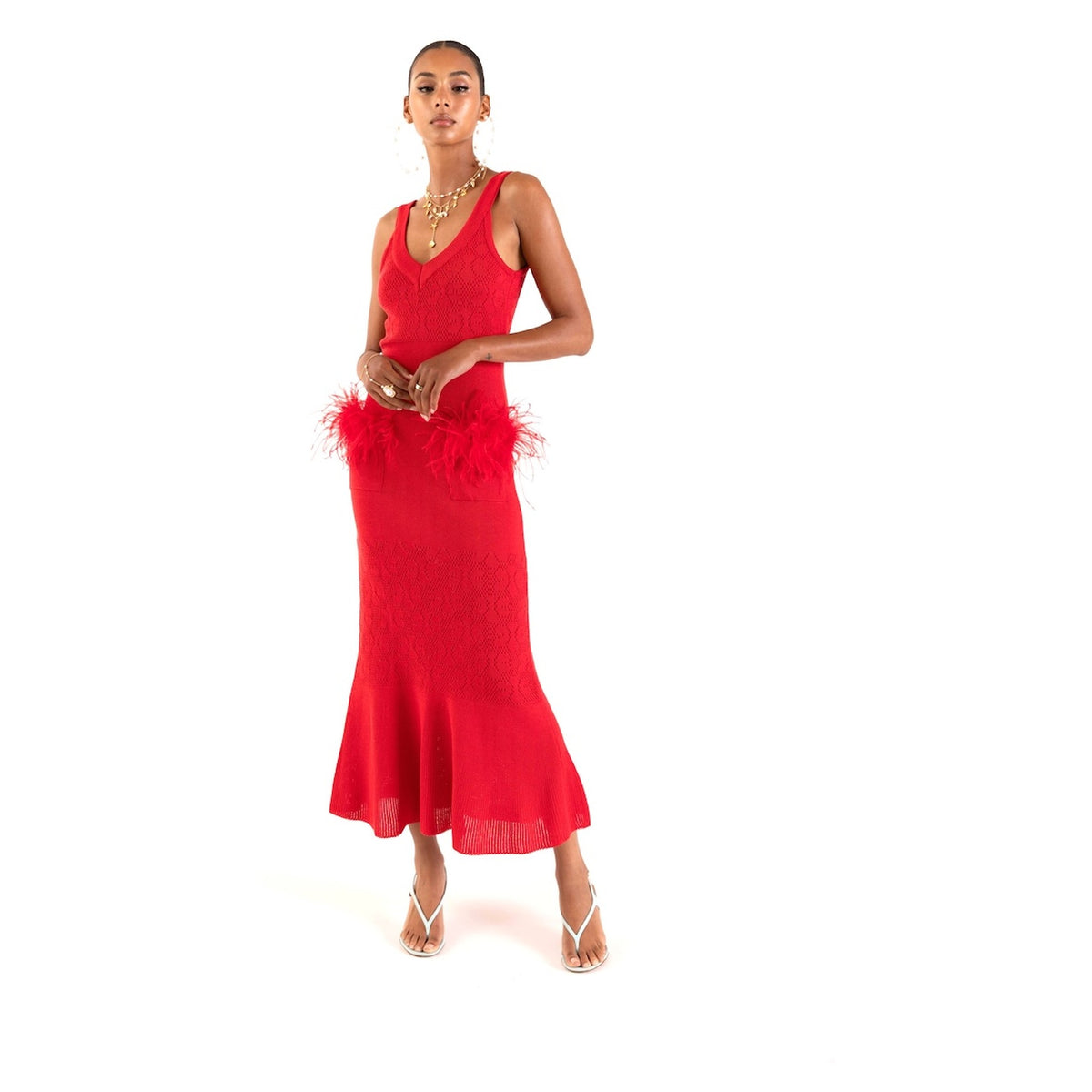A woman poses against a white background wearing the ANDREEVA Cherry Knit Dress With Feather Details, layered necklaces, hoop earrings, and strappy sandals.