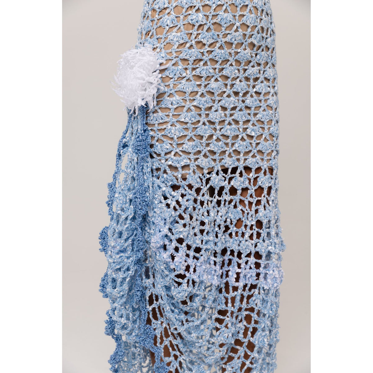 Blue crocheted shawl with white flower detail on a neutral background