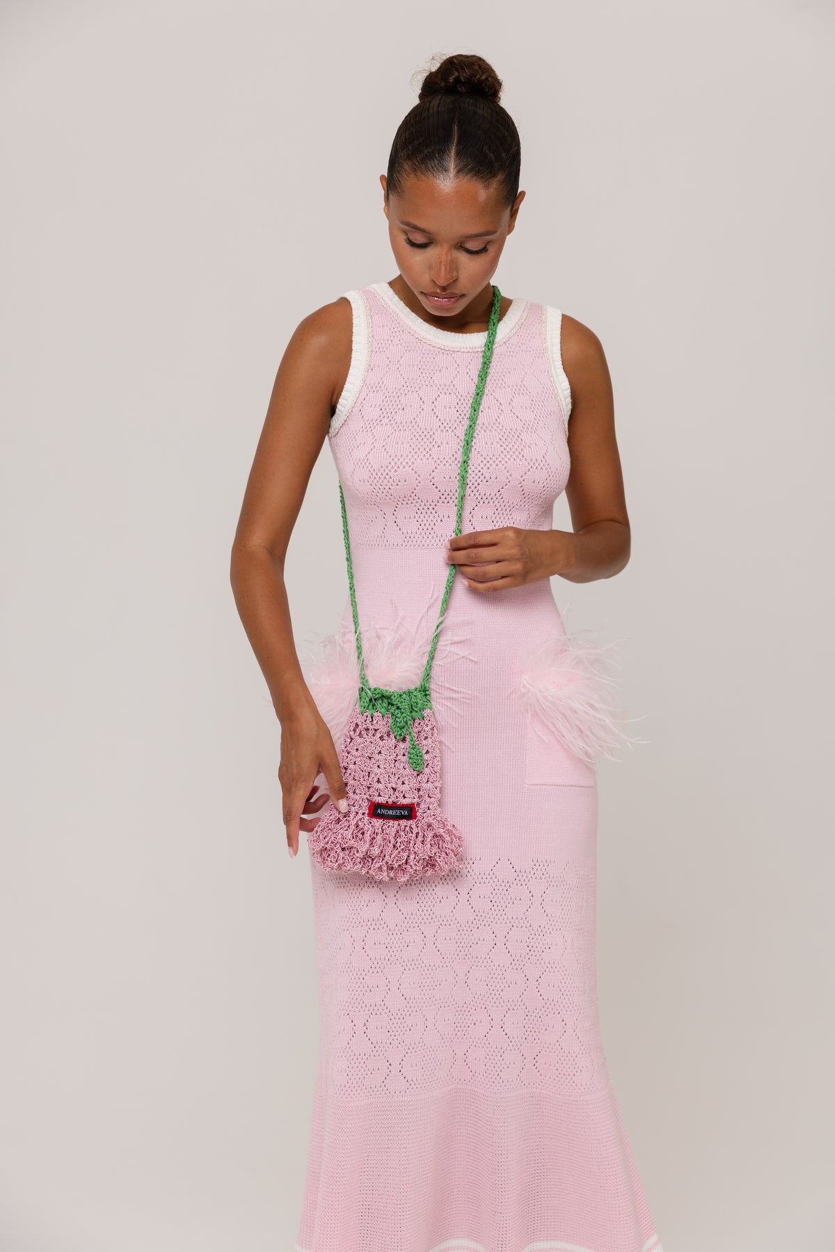 Woman in a pink dress holding a green handbag with a floral pattern against a plain background