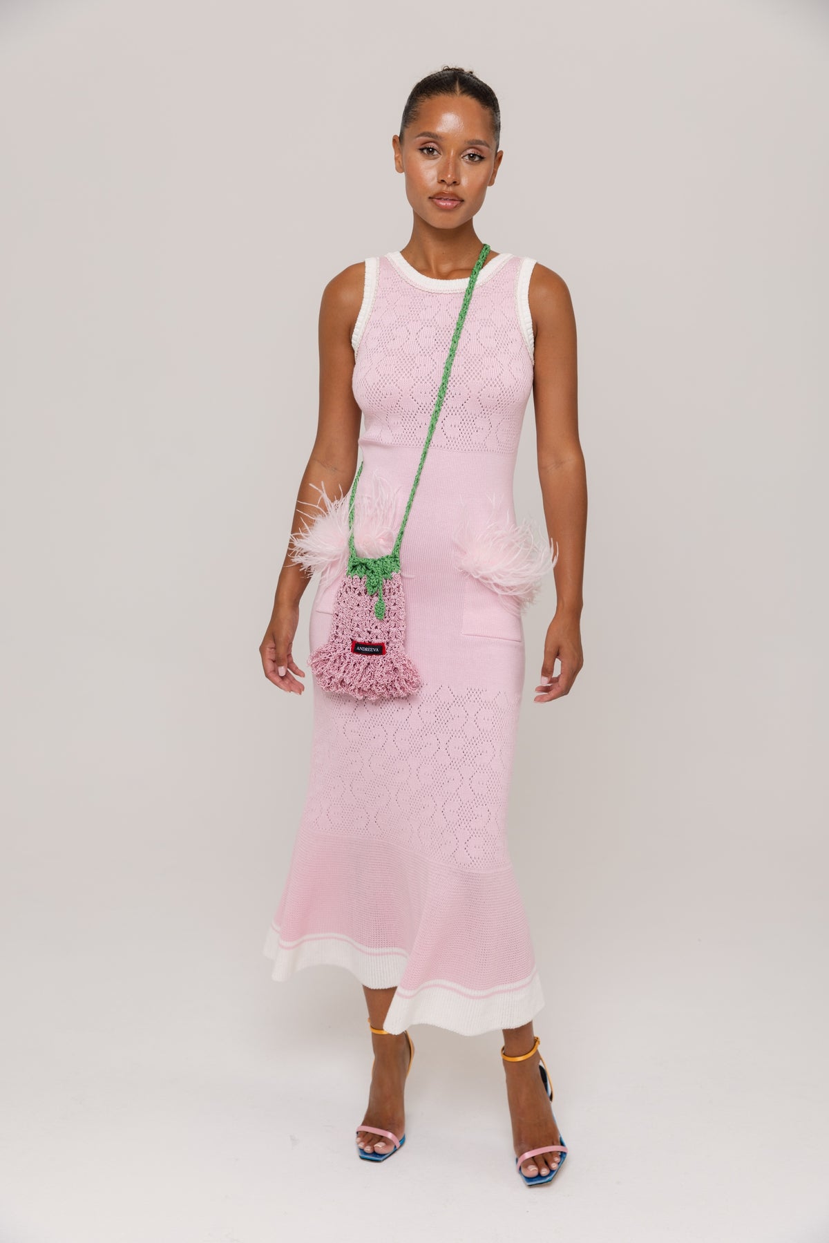 Woman wearing a pink dress with a green bag on a white background