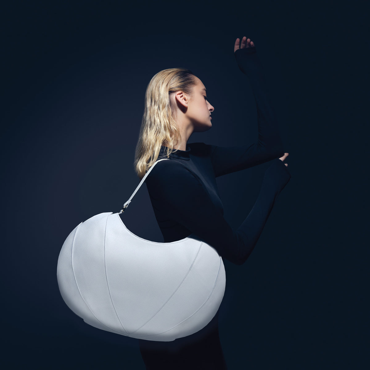 Woman holding a large white spherical object against a dark background
