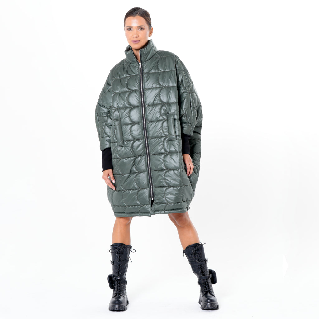 A woman stands against a white background wearing the METAMORPHOZA Oversized Balloon Coat with Voluminous Silhouette, featuring a quilted design and high collar, paired with black lace-up combat boots. Her hair is pulled back and her hands are at her sides.