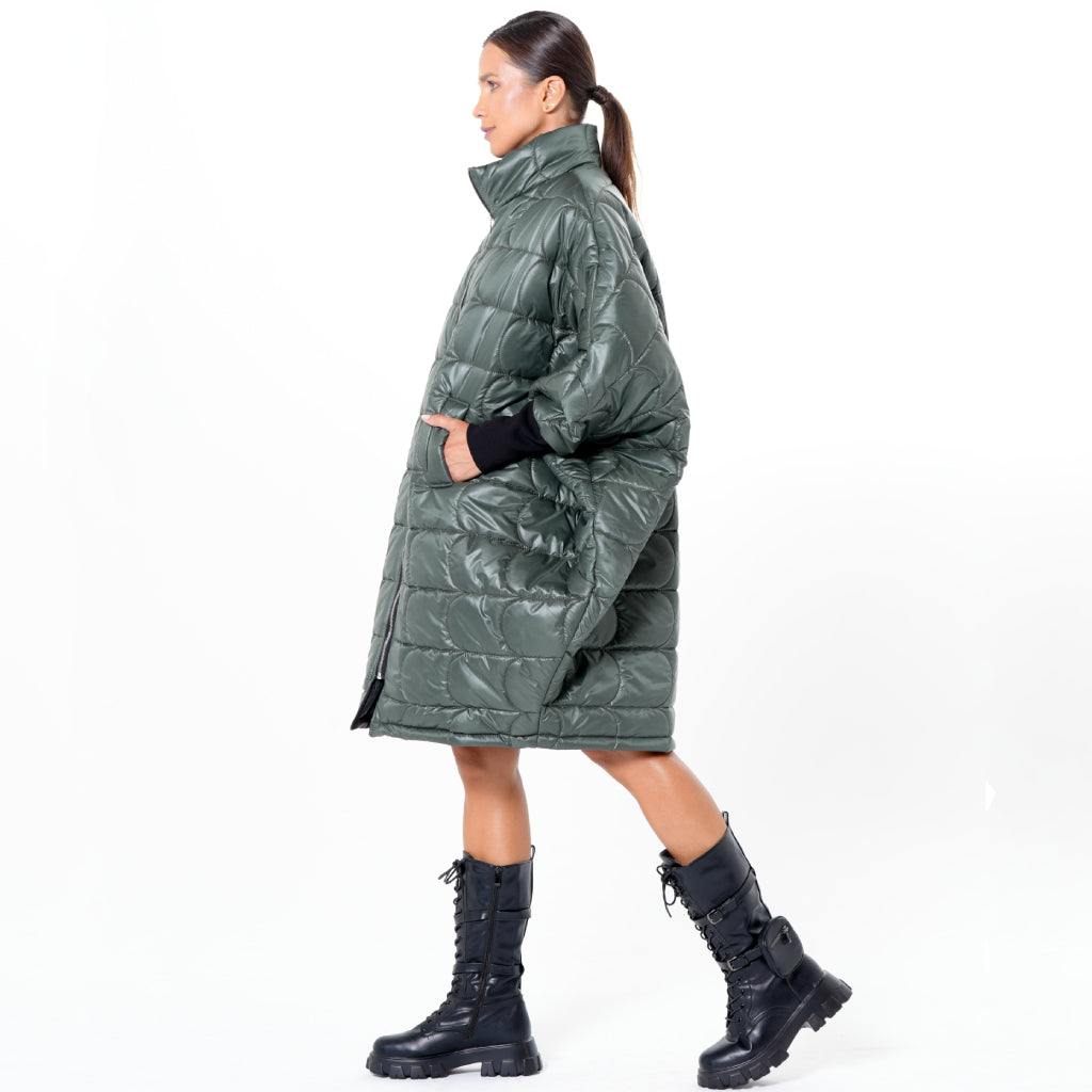 A woman stands in profile against a white background, wearing the METAMORPHOZA Oversized Balloon Coat with Voluminous Silhouette, her hands in the pockets, paired with black lace-up combat boots and her hair tied back in a ponytail.