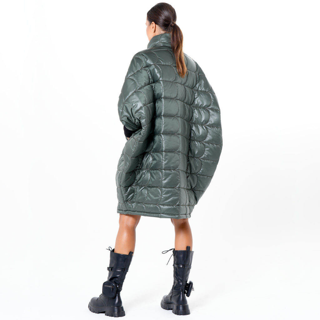 A person with long brown hair in a ponytail models the METAMORPHOZA Oversized Balloon Coat with Voluminous Silhouette in dark green, featuring a quilted design, paired with black boots, standing against a plain white background.