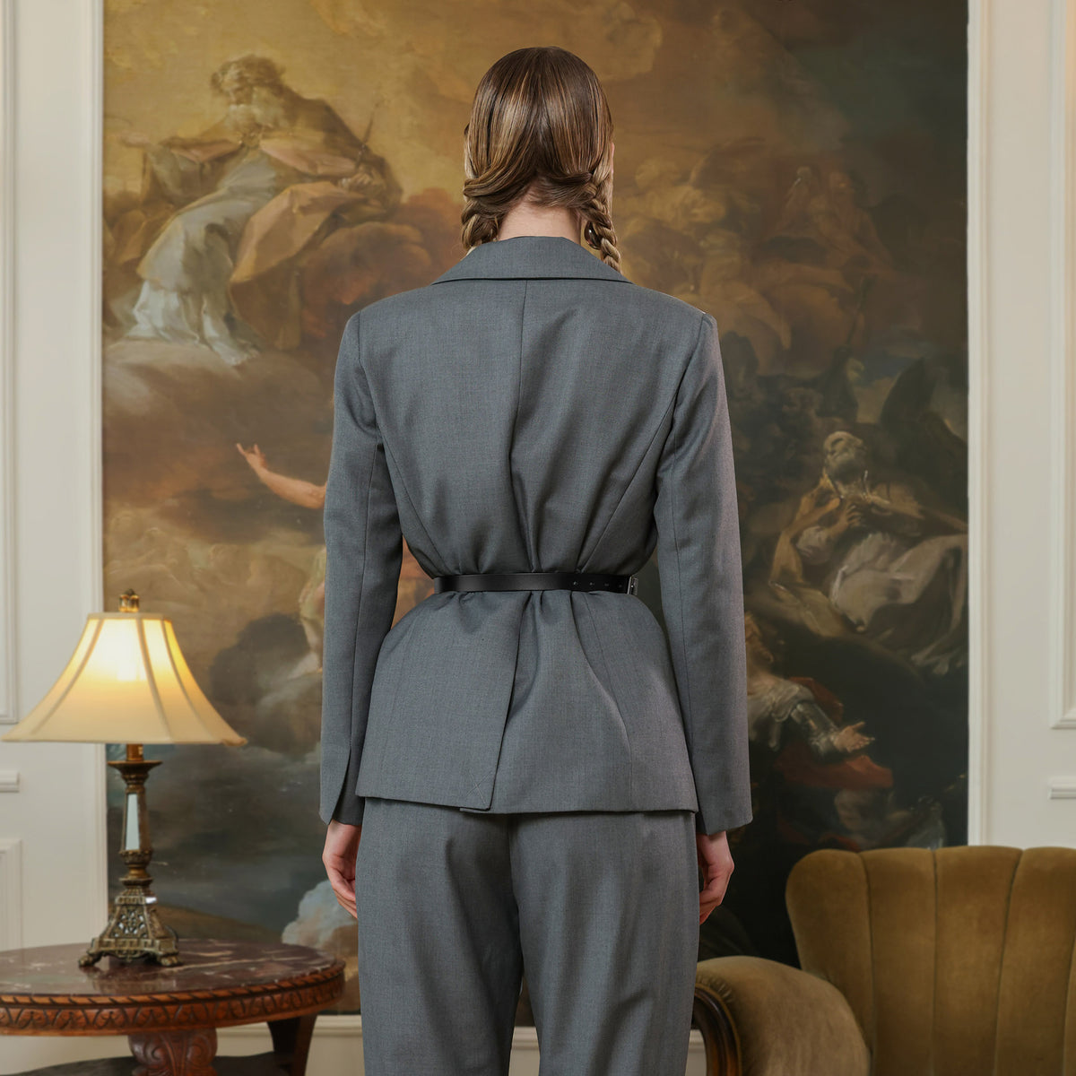 Person wearing a gray suit standing in a room with a large painting on the wall.