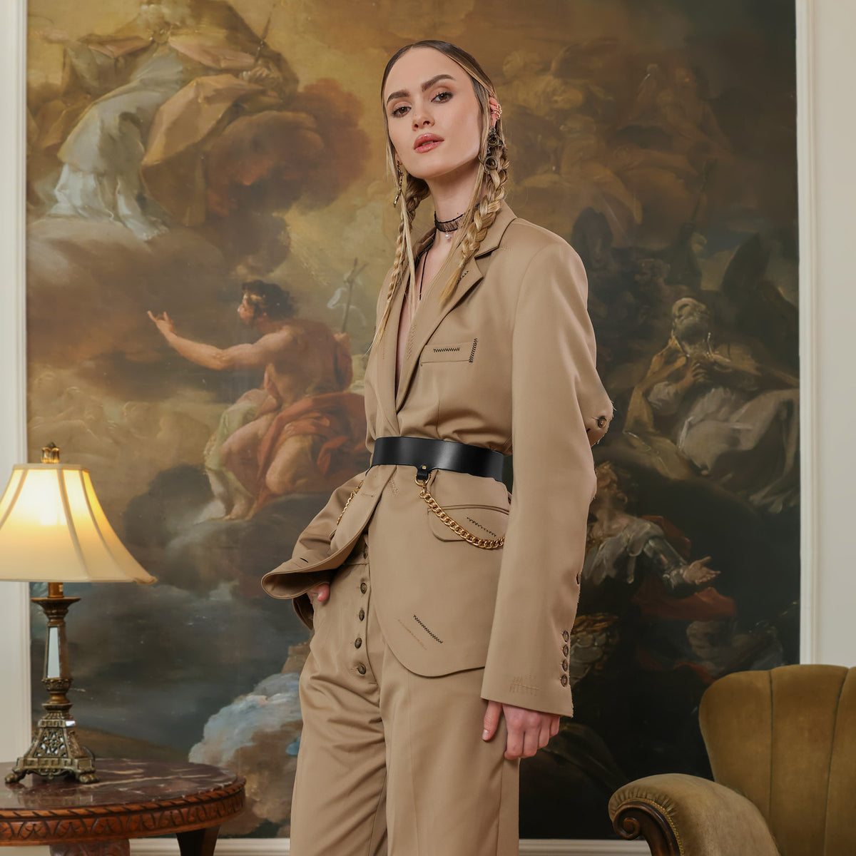 Woman in a beige suit standing in a room with classical painting in the background