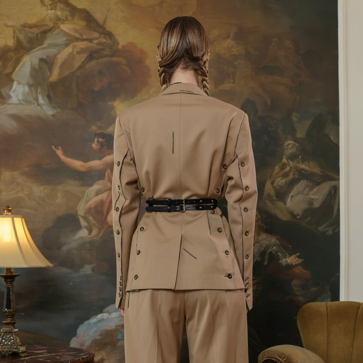 Person wearing a beige trench coat standing in front of a classical painting