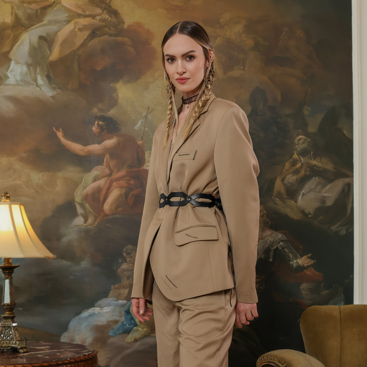 Woman in a beige suit standing in a room with classical painting on the wall