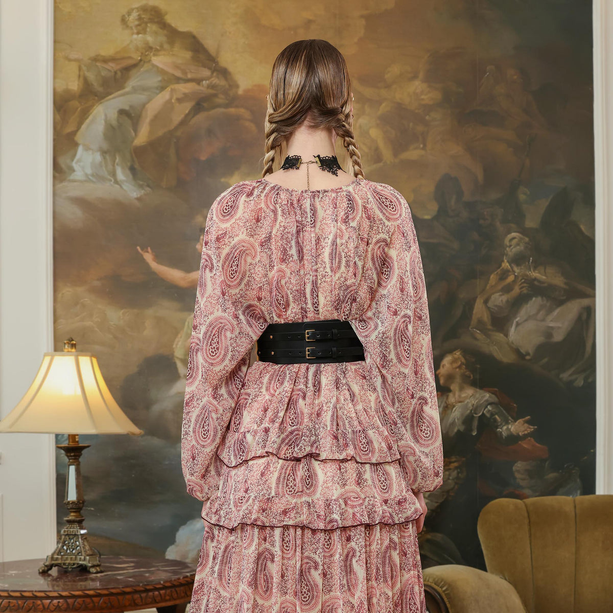 Woman in a patterned dress standing in a room with classical painting on the wall.