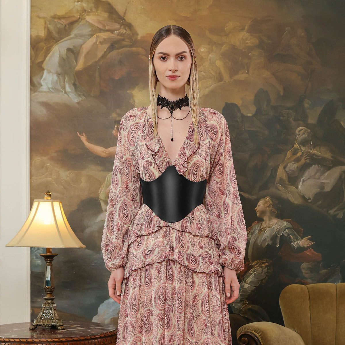 Woman in a patterned outfit standing in front of an ornate painting with black corset