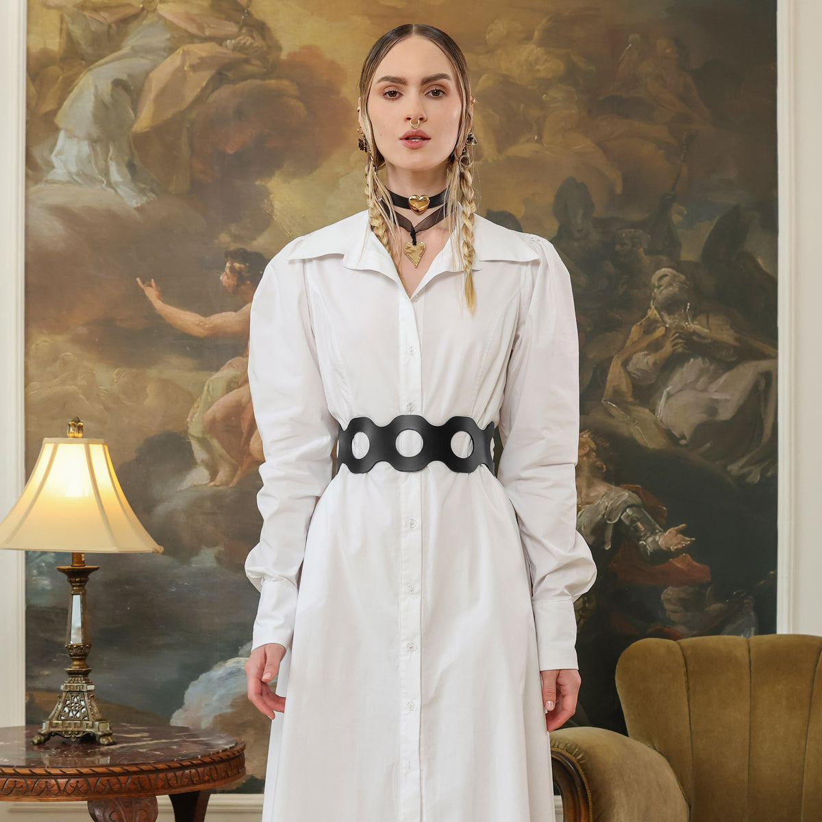 Woman in a white dress with a black belt standing in front of an ornate painting.