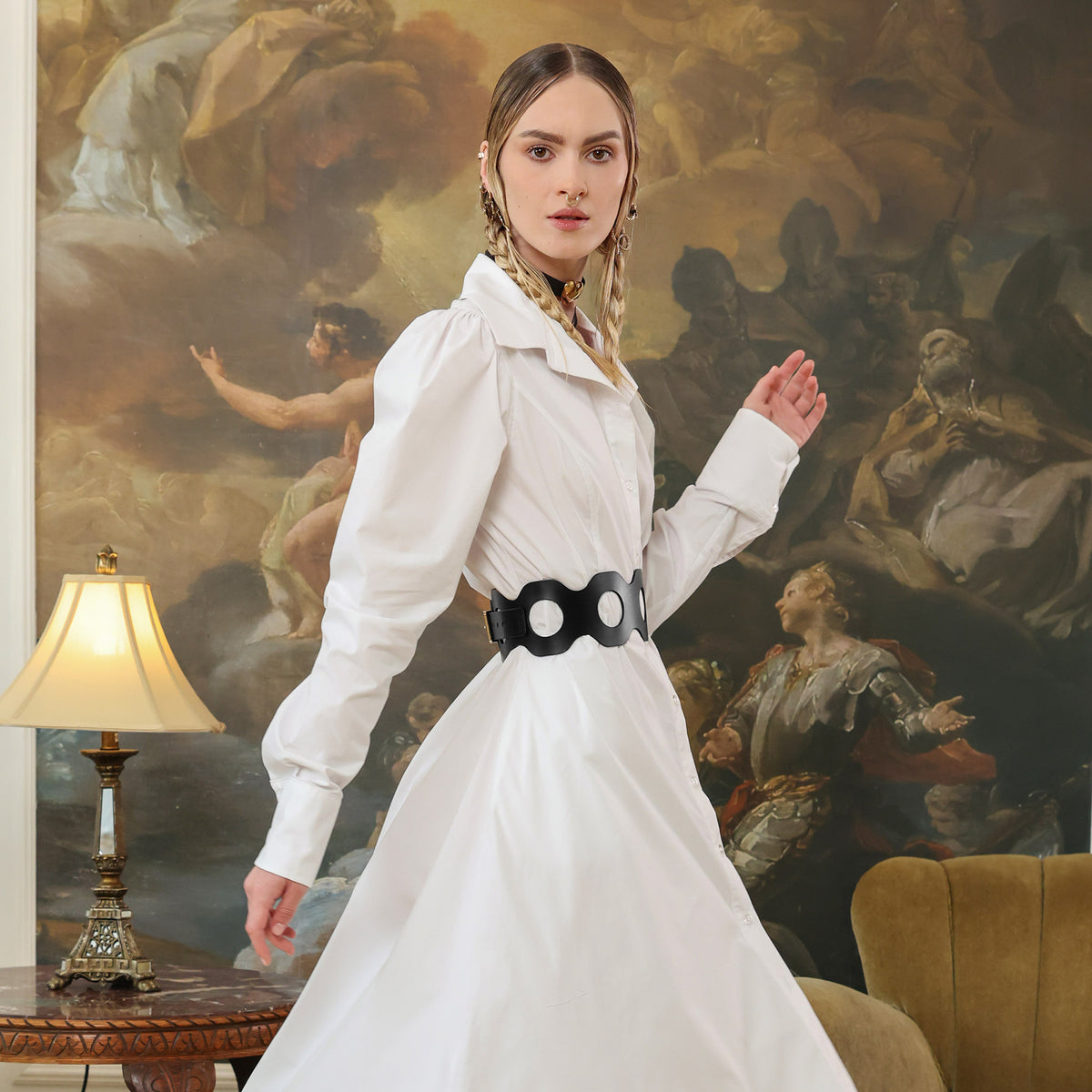 Woman in a white dress with black belt standing in front of a classical painting