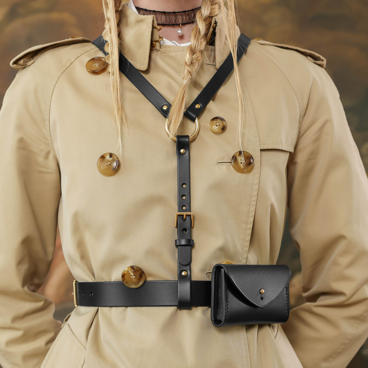 Woman in a beige trench coat standing in front of a classical, black leather harness with a belt and pouchpainting