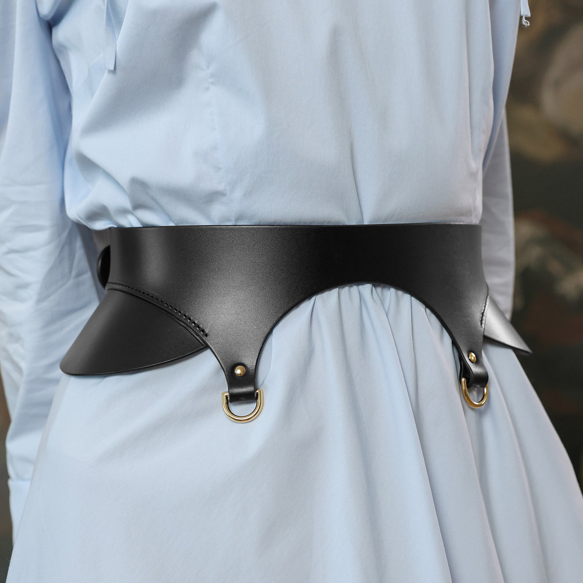 Person wearing a light blue dress with a black leather belt featuring gold hardware.