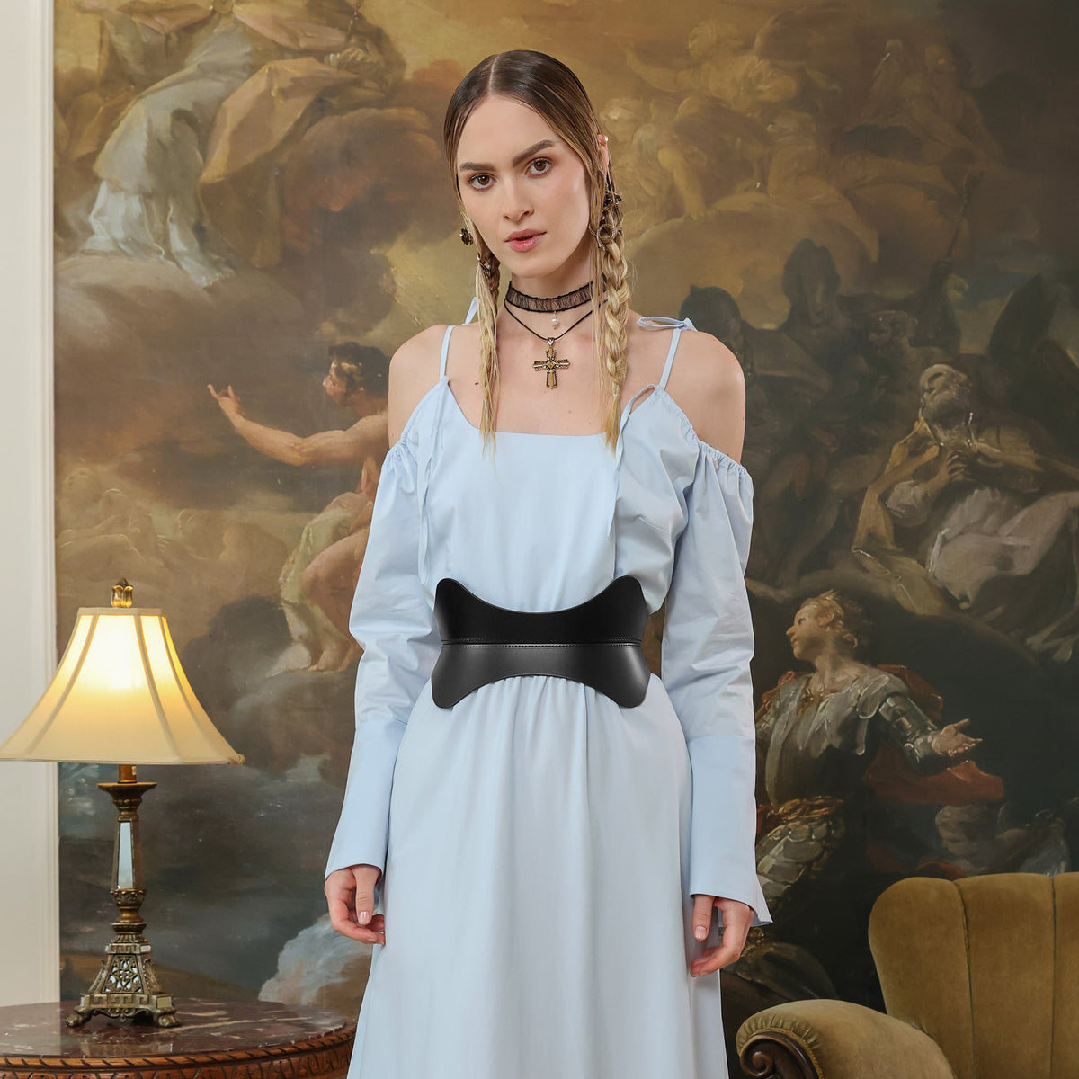 Woman wearing a light blue dress with a black belt in front of a classical painting