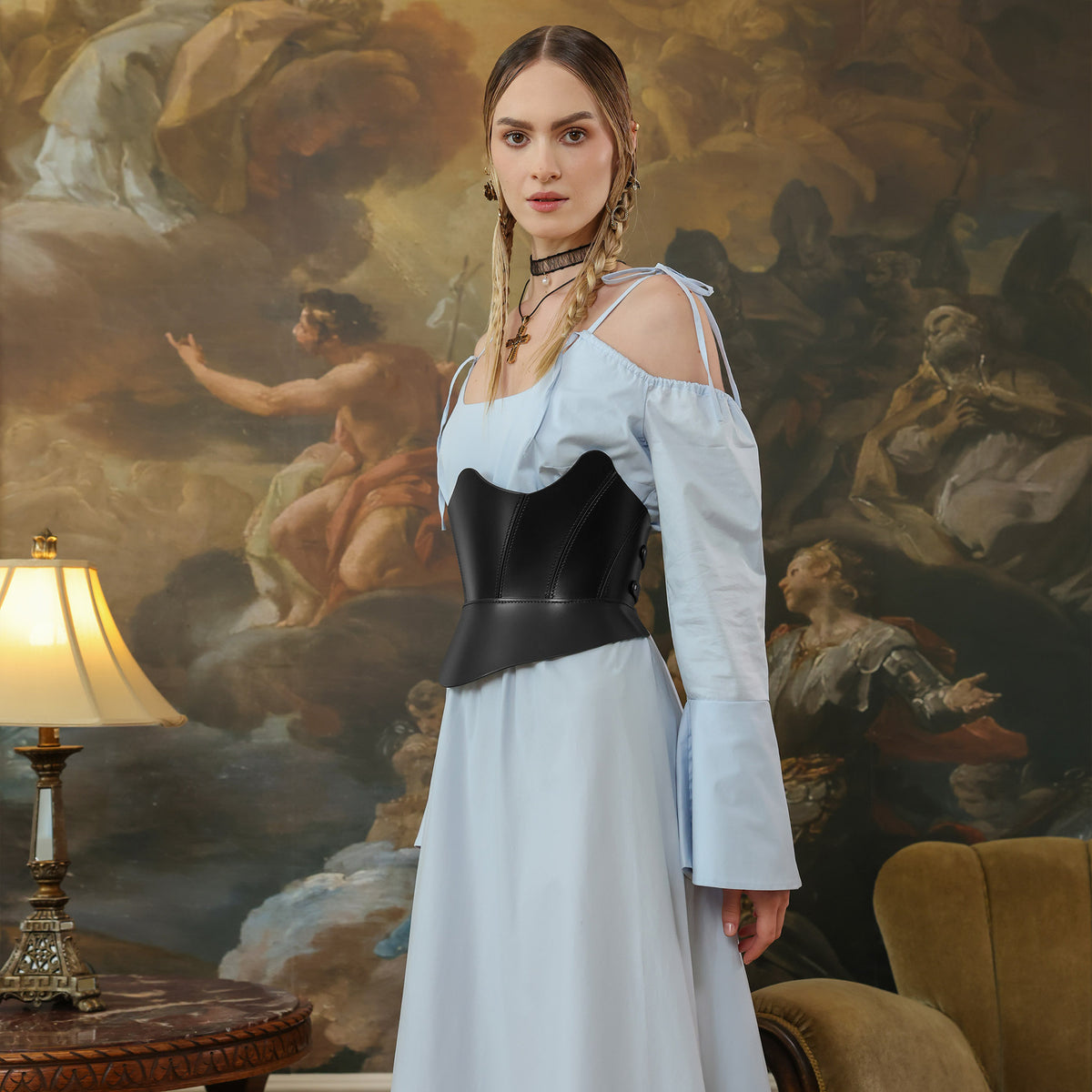 Woman in a white dress with a black corset standing in front of a classical painting.