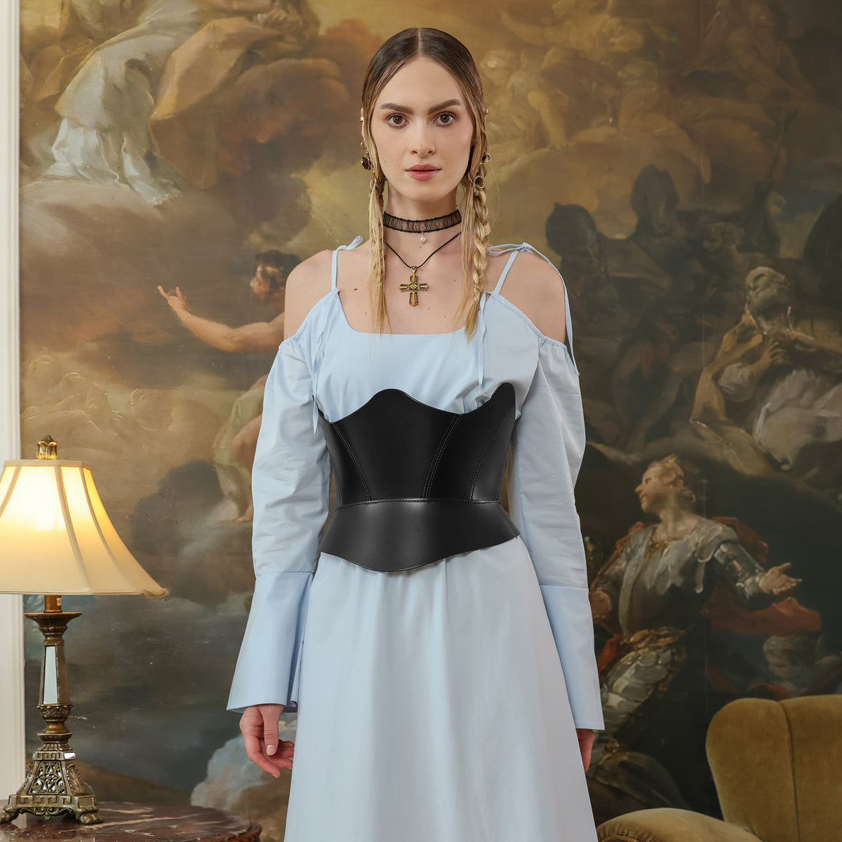 Woman in a light blue dress with a black corset standing in front of a classical painting.