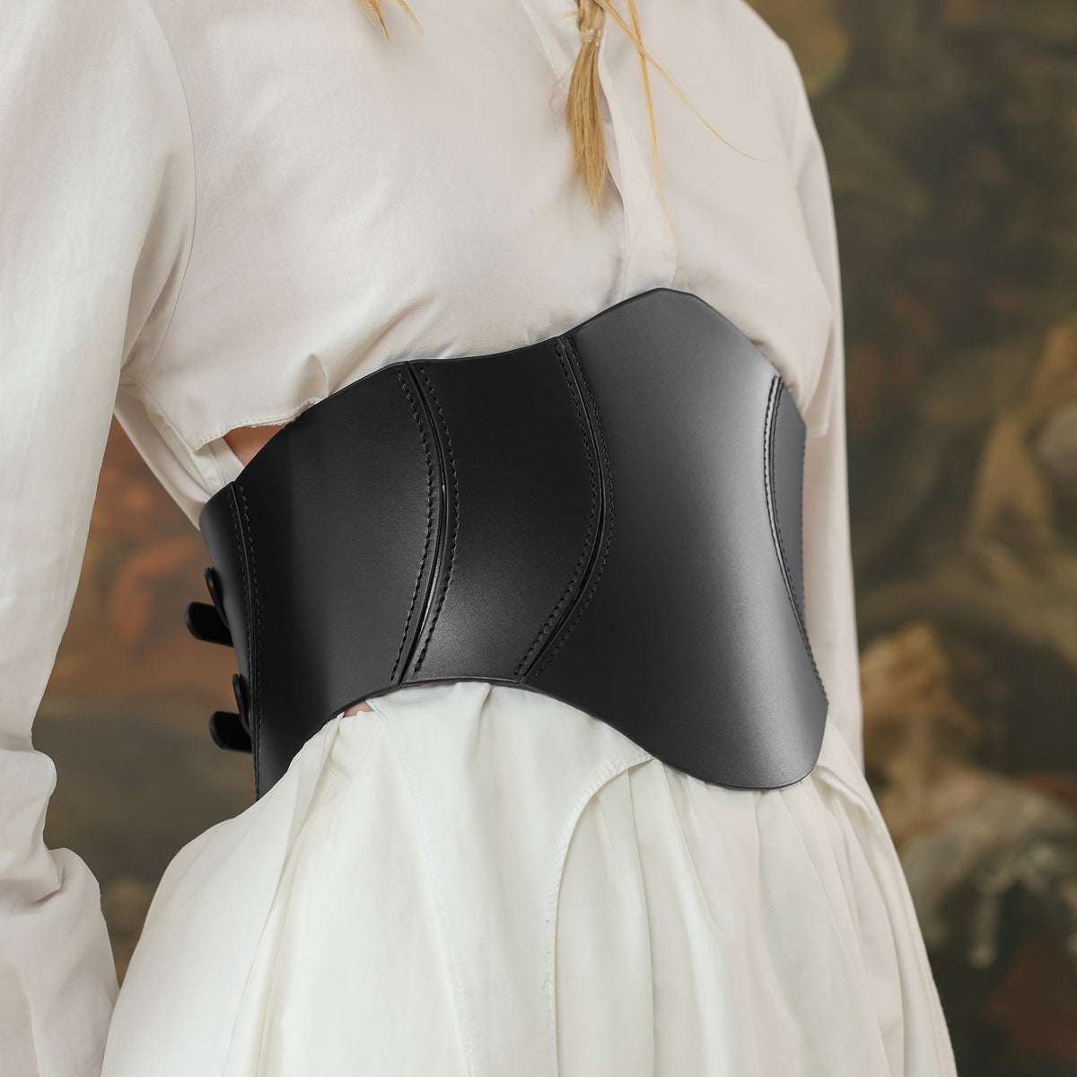 Person wearing a black leather corset belt over a white garment with a blurred background