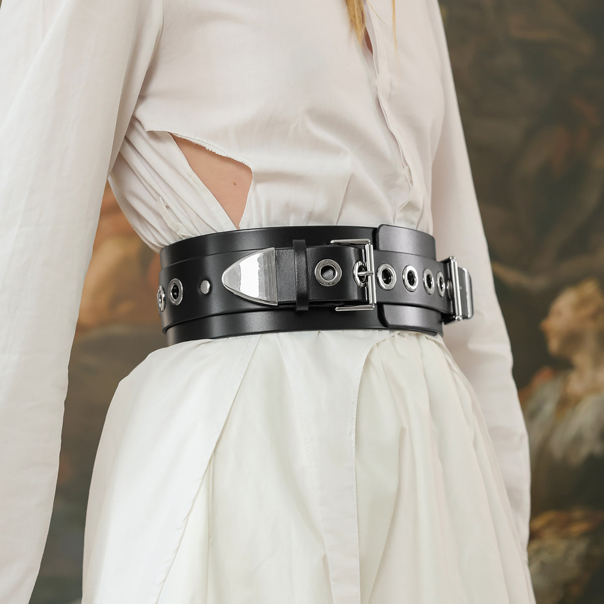Black leather belt with metal accents worn by a person in a white outfit against a blurred background