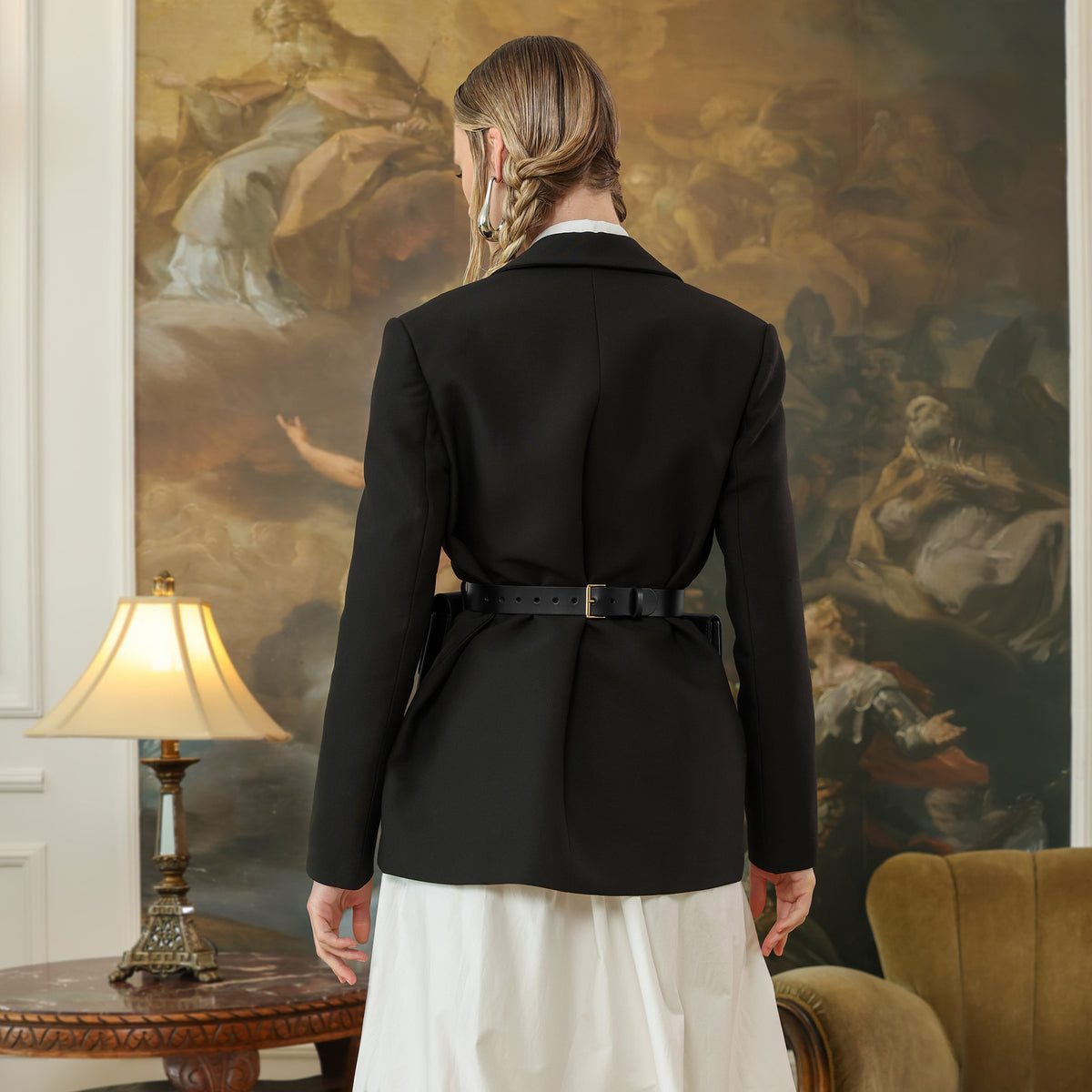 Person wearing a black blazer in an elegant room with a painting in the background