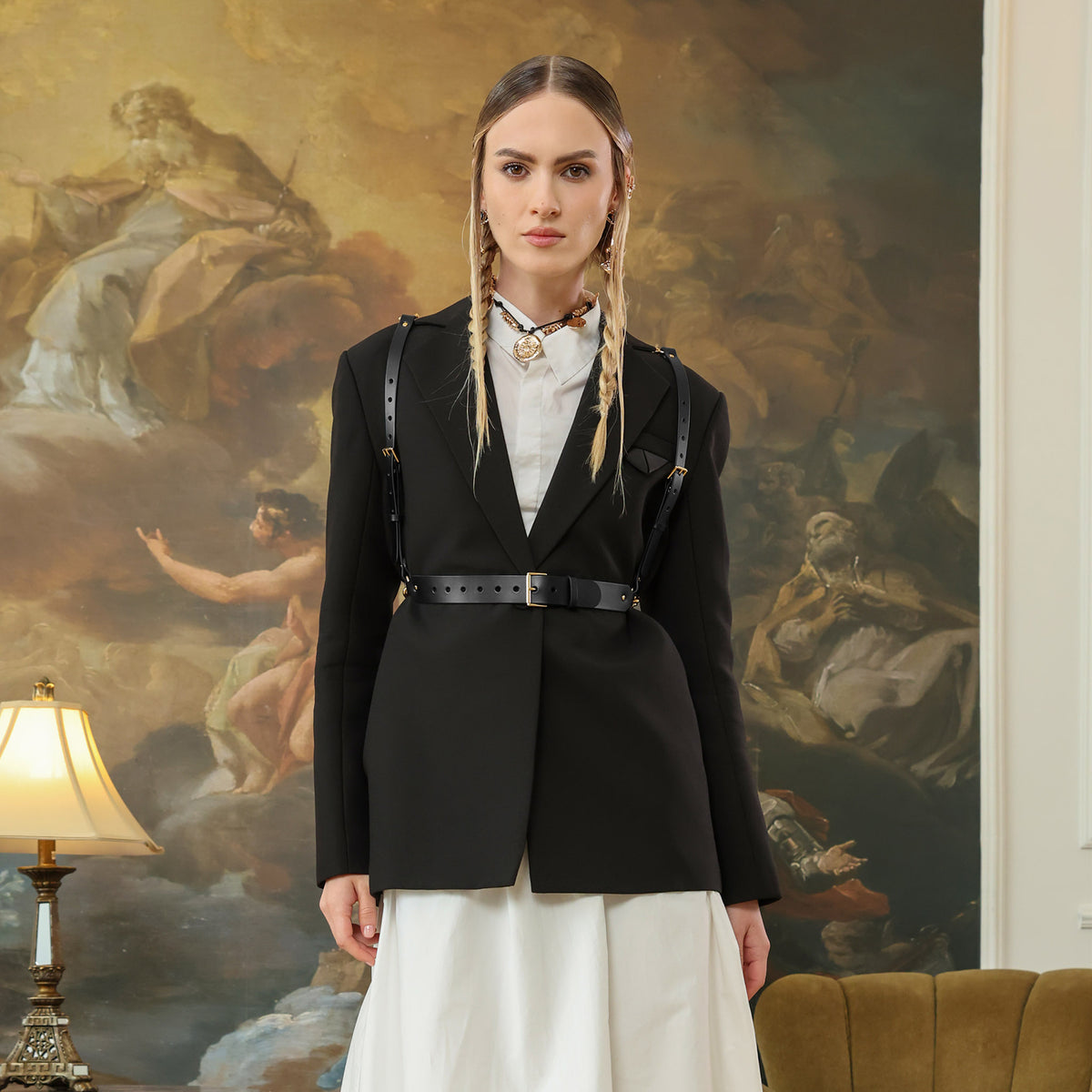 Woman in a black blazer and white dress standing in front of classical painting