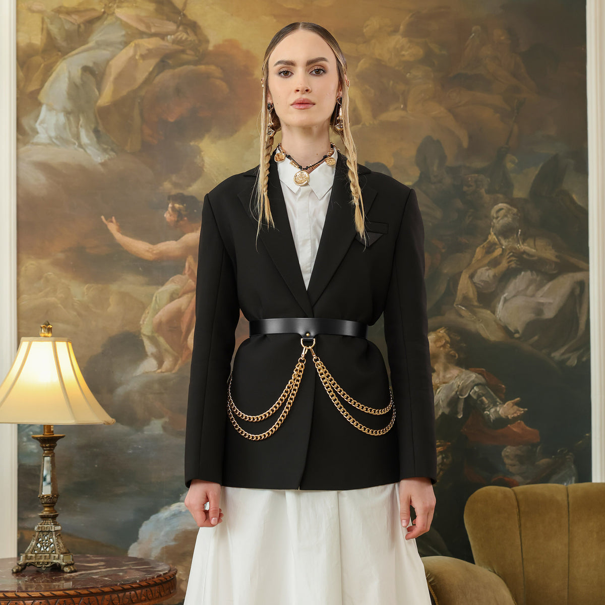 Woman wearing a black blazer with gold chains in front of a classical painting